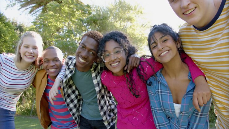 Portrait of happy diverse group of teenage friends embracing in sunny park, slow motion