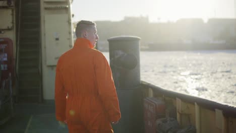 Trabajador-Portuario-Con-Uniforme-Naranja-Parado-Junto-Al-Tablero-Del-Barco.-Destello-De-Lente.-Camara-Lenta