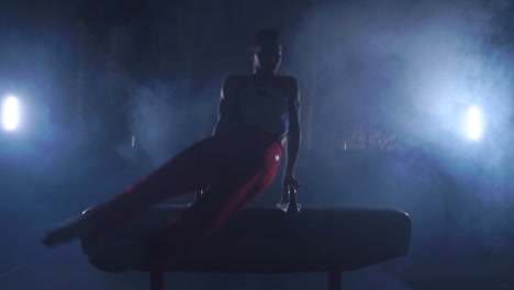 male gymnast athlete performs handstand and spin on pommel horse on a dark background and smoke in slow motion. olympic programme