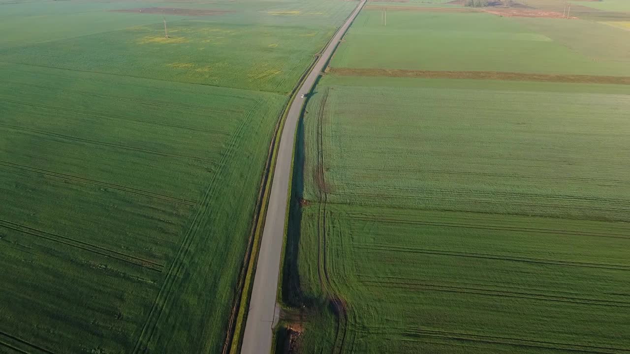 drone volando sobre una pequeña carretera rural con campos de cultivo verdes a los lados