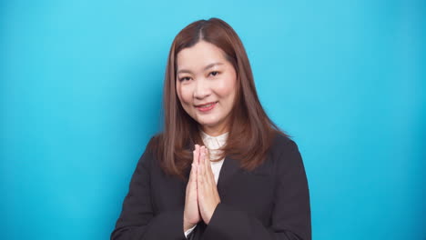 beautiful thai businesswoman in a black suit guests sawadee with a smile on blue background