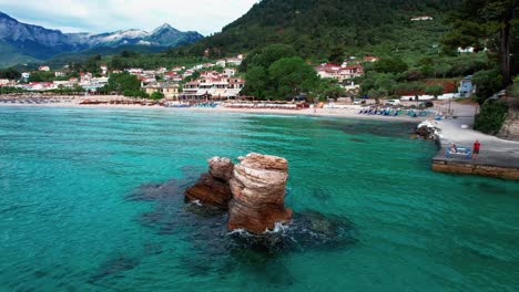 rotating aerial view with a small cliff in the foreground and the famous golden beach in the background with towering mountain peaks, thassos island, greece