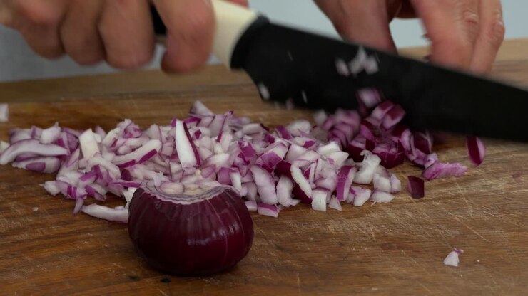 Dicing a red onion in preparation to stir fry on a cutting board