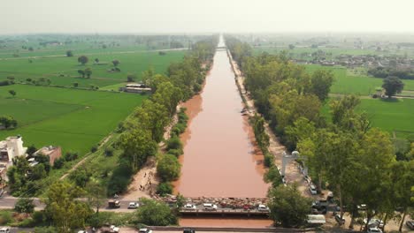 Vista-De-Drones-Del-Río-Fangoso-Que-Fluye-En-Medio-De-árboles-Cerca-Del-área-Agrícola-En-La-Provincia-De-Punjab