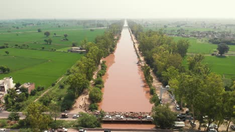 drone view of muddy river flowing in the middle of trees nearby farming area in punjab province
