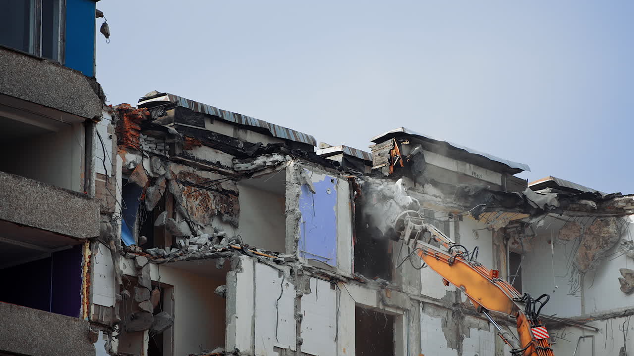 Destruction machine demolishes the ruined building. Pieces of concrete falling down from the roof of the destroyed house. Cleaning the site for the new construction.