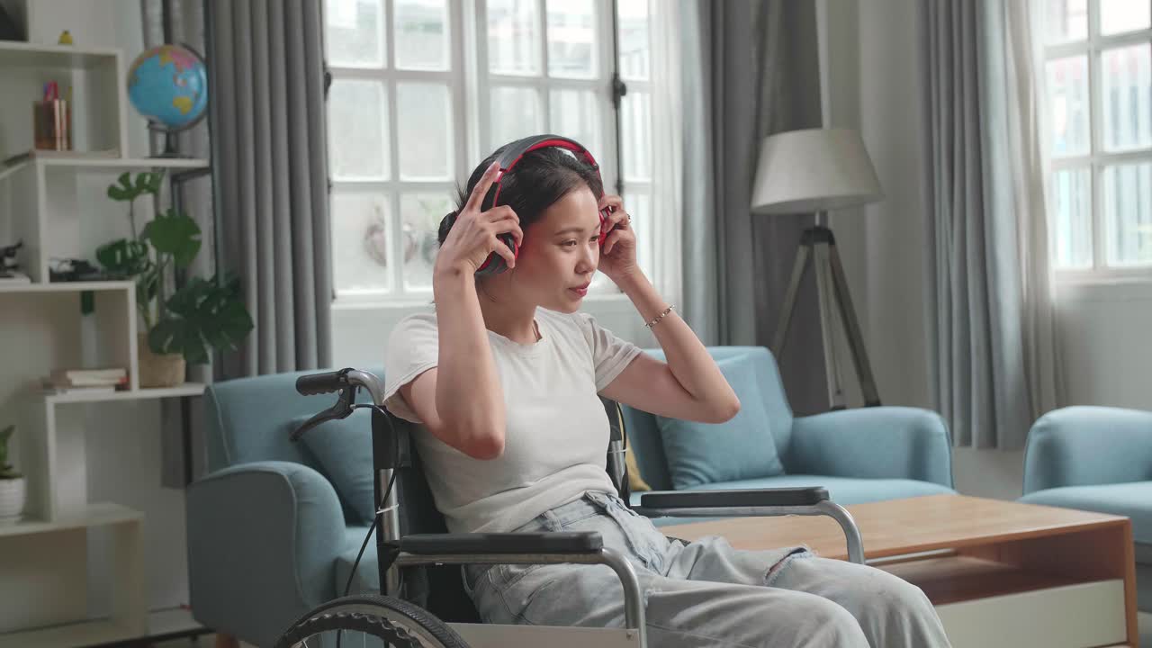 Asian Woman Sitting In A Wheelchair Listening To Music With Headphones In Living Room