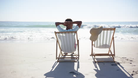 a young biracial man relaxes on a beach chair, facing the ocean, suggesting a moment of tranquility