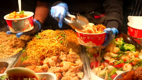 close up of street food market workers with gloves filling pots with noodles and fried chicken in camden town