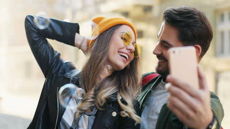 vista de cerca de una joven pareja caucásica de amigos tomándose selfies mientras caen bolas transparentes de jabón