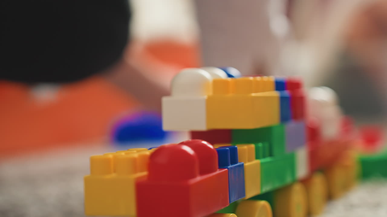 Mother assembles toy train. Mom pieces together bright plastic train on soft carpet surface. Mother carefully assembling lively and colorful toy train using plastic blocks and wheels