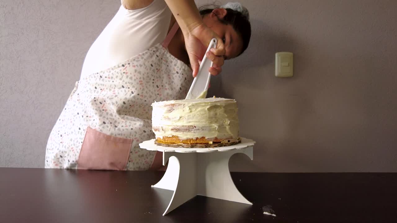 Donna latina con un grembiule che prepara una torta spalmando la glassa al burro con una spatola per torte in plastica bianca