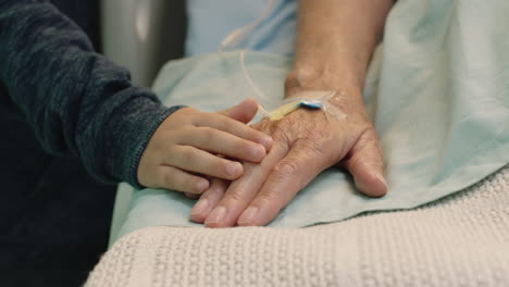 little boy touching hand of grandmother lying in hospital bed child showing affection at bedside for granny recovering from illness health care support