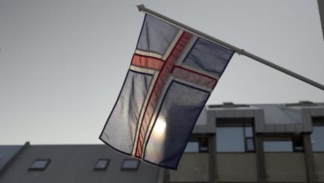 icelandic flag waving in the wind, with buildings behind it, in slow motion, iceland