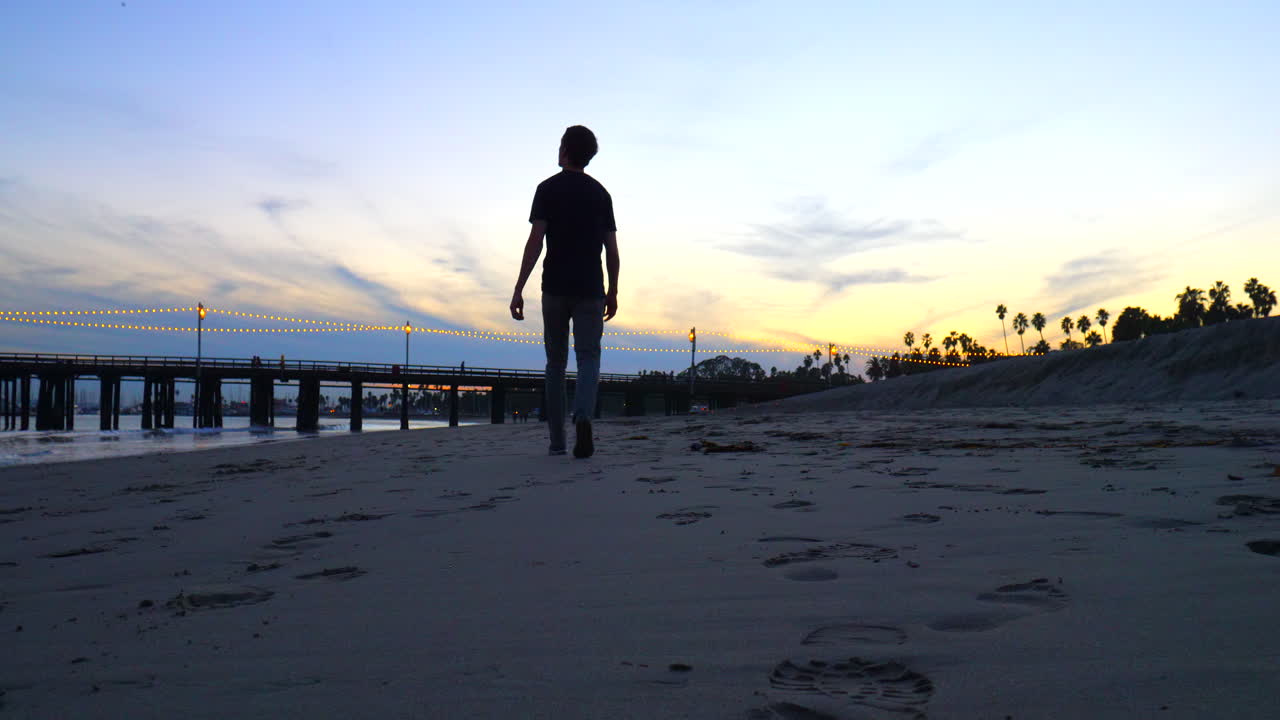 un hombre camina solo en la playa hasta el muelle stearns wharf al atardecer viendo las olas del océano en la orilla en santa barbara, california