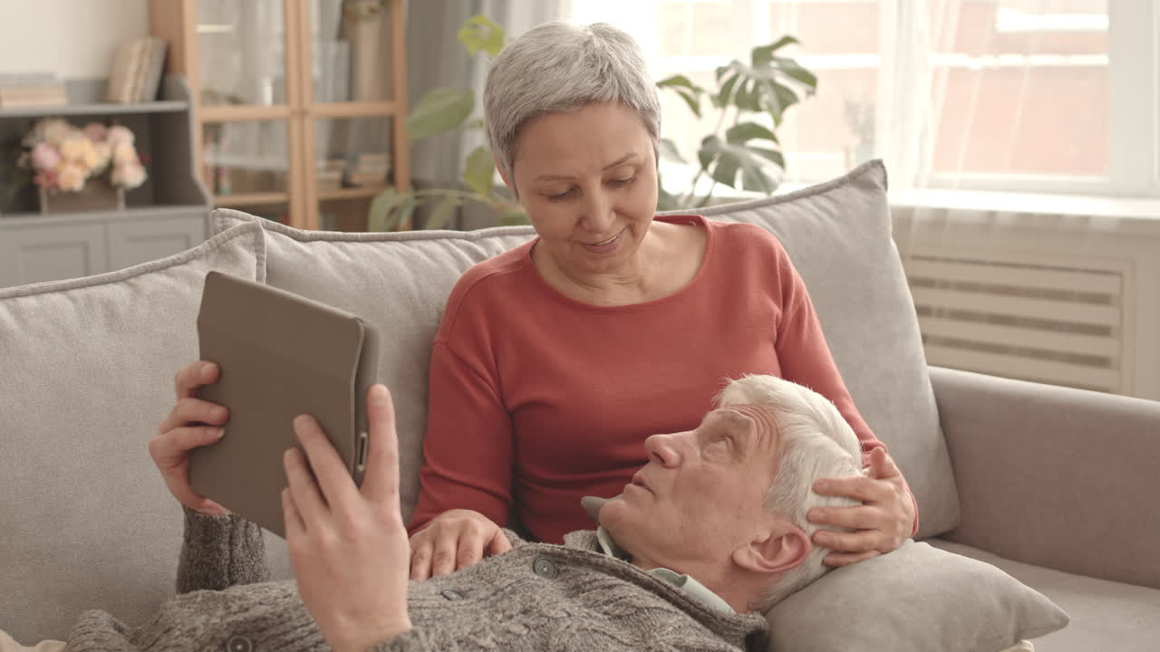 una pareja de ancianos relajándose juntos en el sofá viendo la tableta.