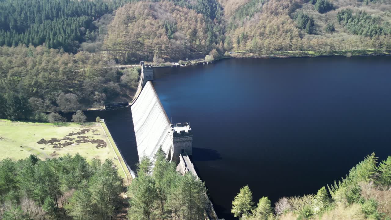 Aerial view of water cascading over the Derwent Dam, in the Peak District, UK with a reveal of the Derwent reservoir towards Howden Reservoir