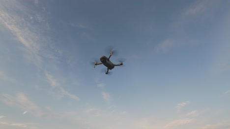 a drone hovers high in the sky, surrounded by white clouds against a backdrop of bright blue sky