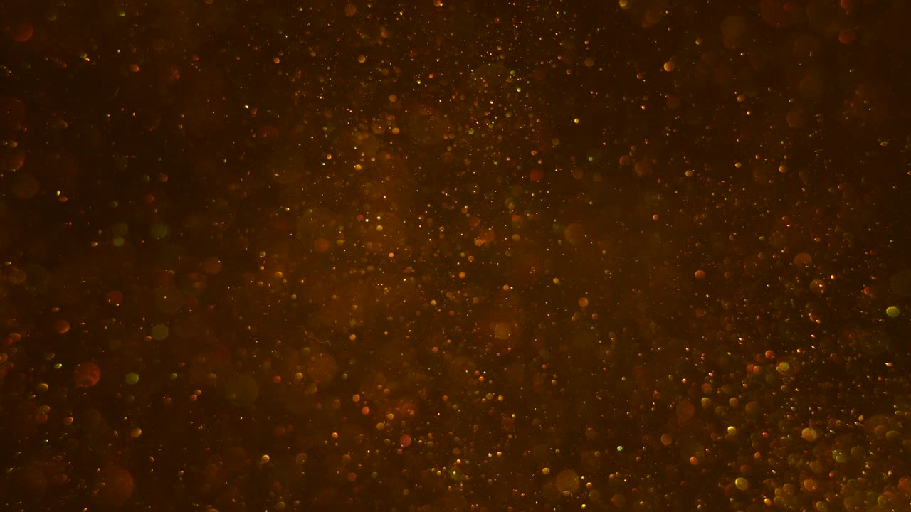 burbujas de bokeh dorado y pequeñas partículas de polvo brillantes moviéndose suavemente arriba y abajo en el fondo oscuro.