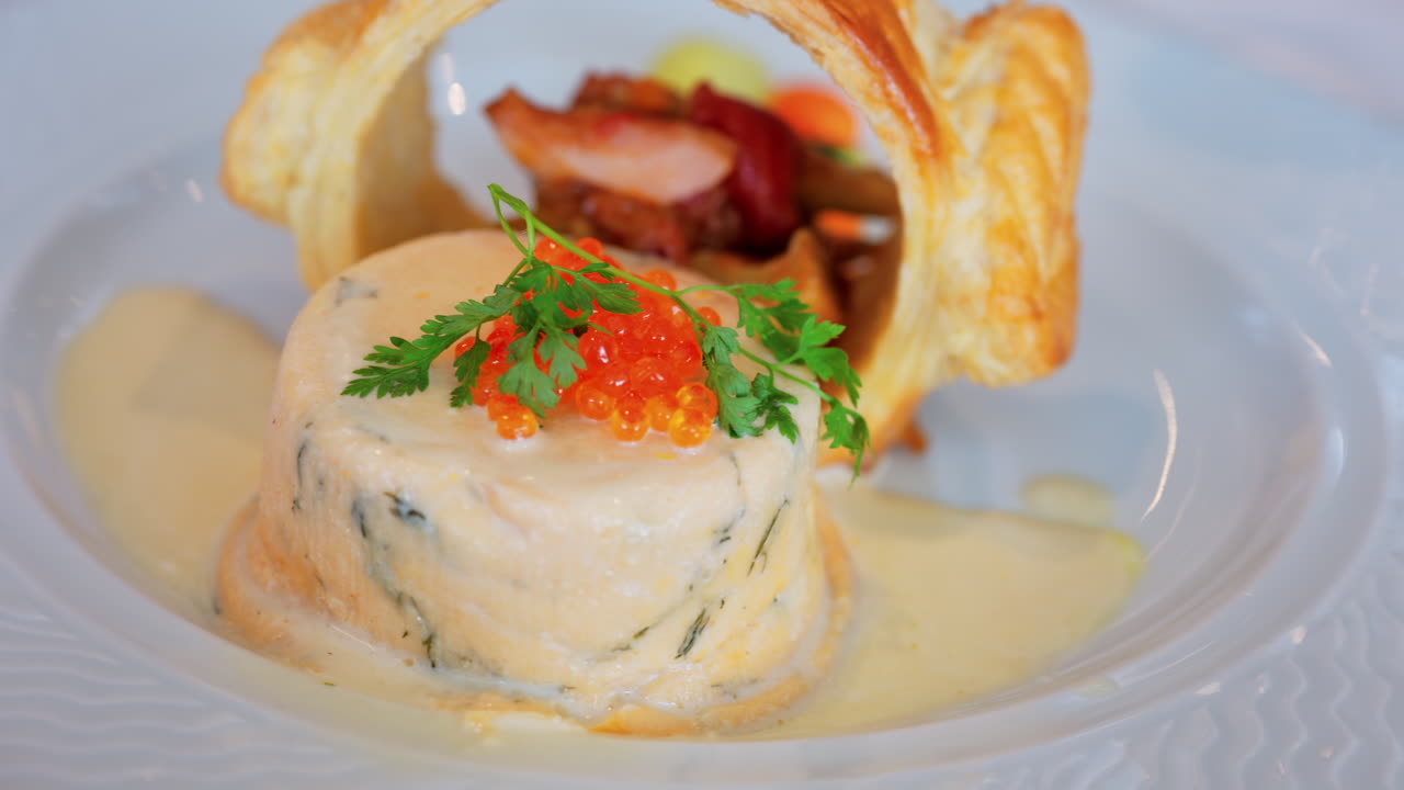 Close up of a fish mousse with salmon roe and puff pastry on a white plate at a restaurant