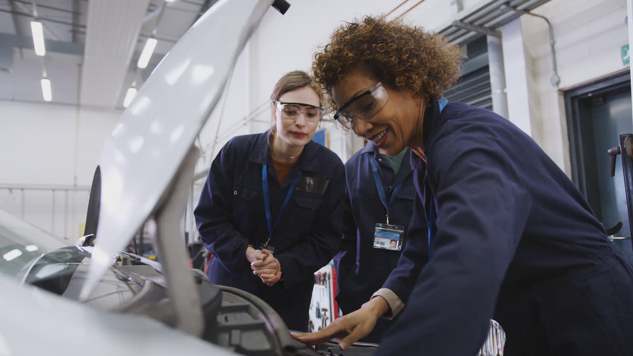 tutora con estudiantes comprobando el nivel de aceite en el motor del coche en un curso de mecánica de automóviles en la universidad