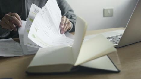 Closeup-Slow-motion-elder-caucasian-woman-hands-pass-through-paper-bills-office-laptop-organizer,-accounting-home-payments-concept-next-to-laptop