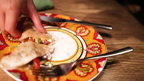 a hand grabs a slice of mexican pizza from a colorful plate, set on a wooden table with warm lighting