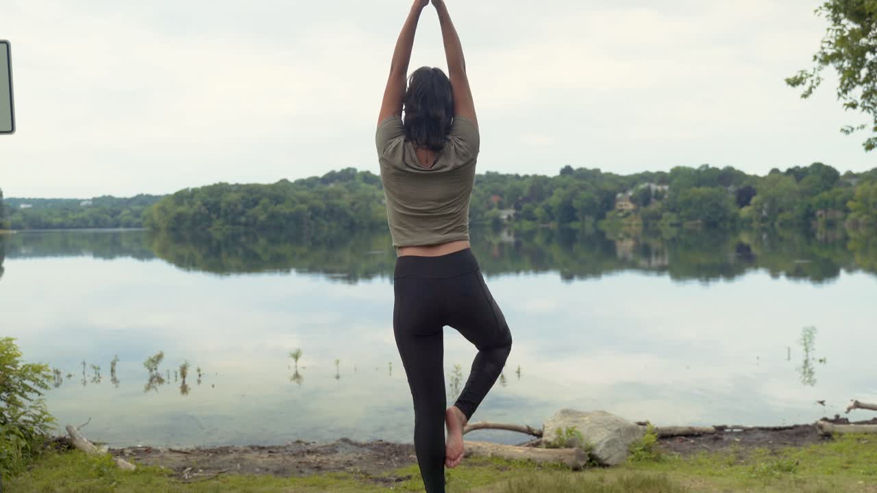 mujer latina relajada practicando yoga en pose de árbol meditando en roca junto a estanque