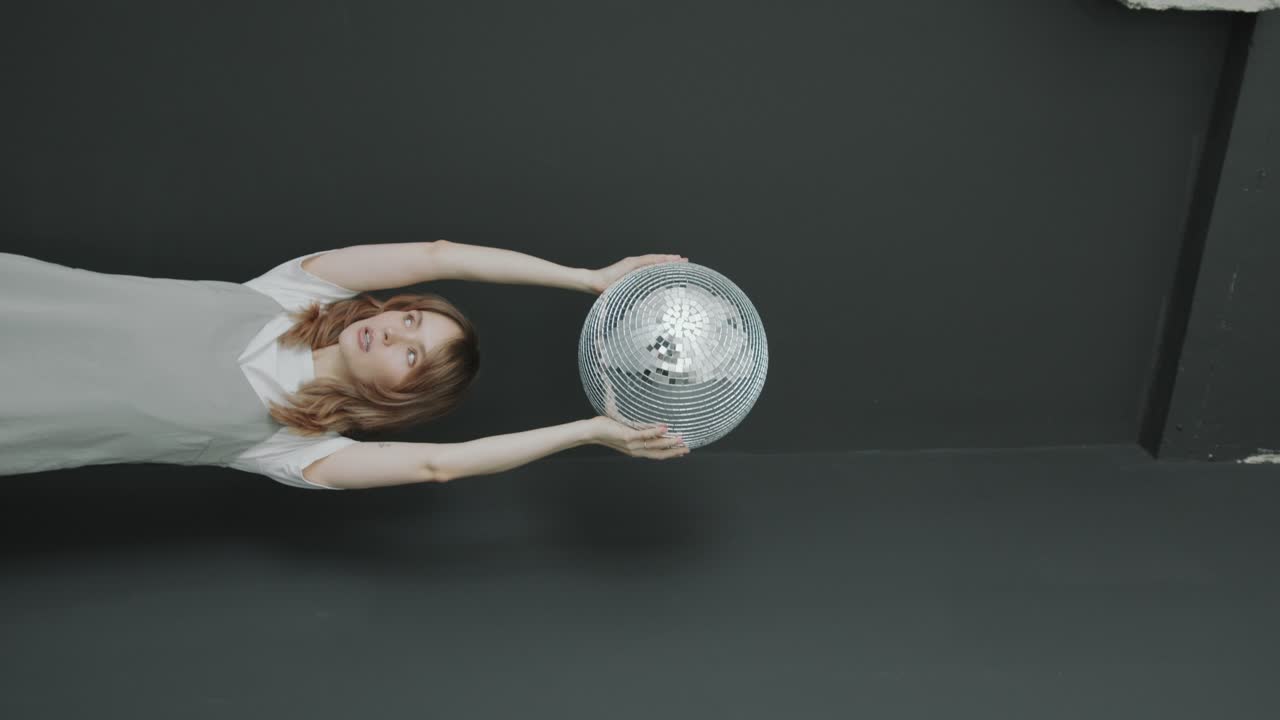 Young Woman Posing with Disco Ball above Head during Studio Photo Shoot