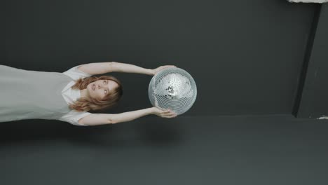young woman posing with disco ball above head during studio photo shoot
