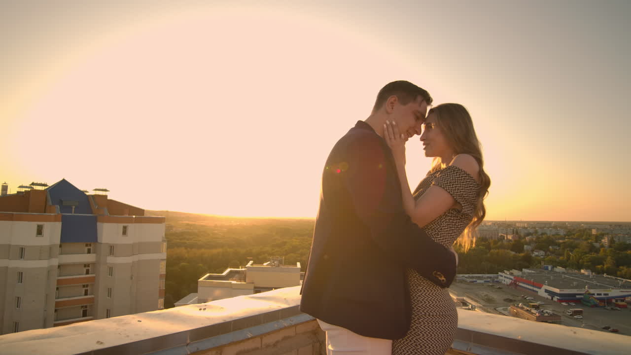 Young couple in love standing on the roof hug and closely look at each other. Romantic evening on the roof of the building. A date on the roof of a building love. Slow motion
