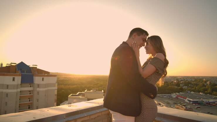 Young couple in love standing on the roof hug and closely look at each other. Romantic evening on the roof of the building. A date on the roof of a building love. Slow motion