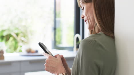 Middle-aged-Caucasian-woman-checks-her-phone-at-home,-with-copy-space