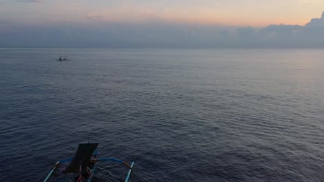 Zoom-Aéreo-Fuera-Del-Interminable-Océano-Azul-Con-Un-Solo-Barco-Jukung-Indonesio-En-El-Horizonte-Al-Amanecer-En-Lovina-Bali-Indonesia