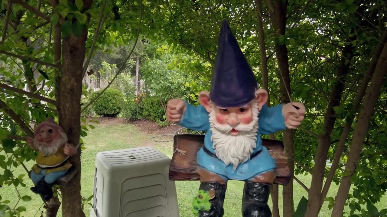 Paesaggio di giardino lussureggiante con statue di gnomi decorative, piante tropicali, vasi di fiori sospesi e alberi verdi in un ambiente esterno tranquillo in Messico.