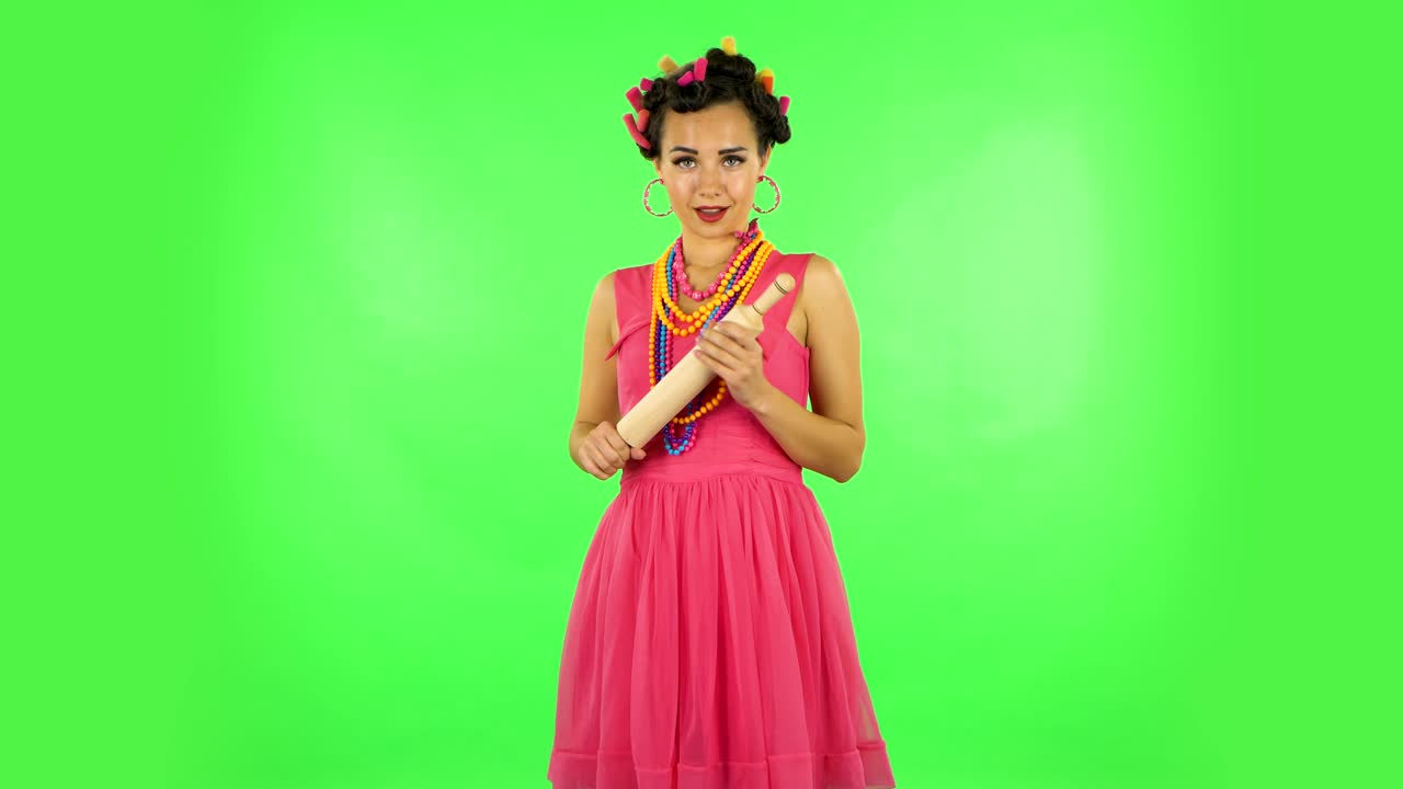 Girl with a rolling pin in her hands seductively looks at the camera. Green screen