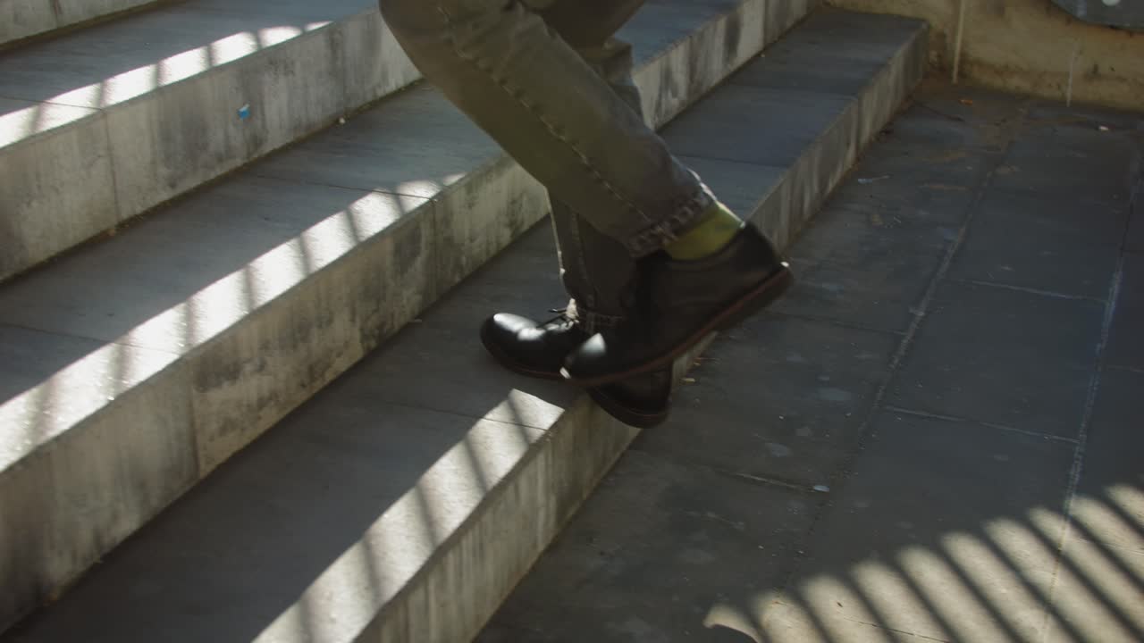 A man is seen ascending concrete stairs, with long shadows from sunlight on a striped pattern cast on the steps