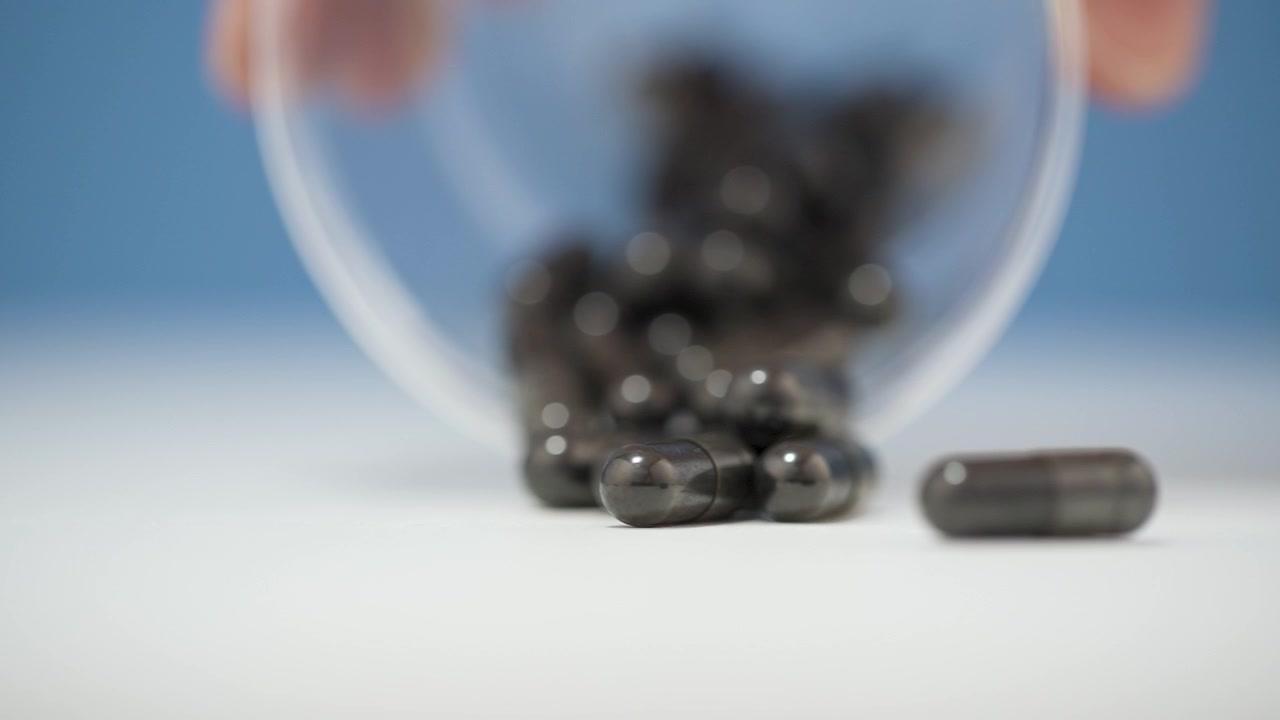 Versamento di capsule nere da una tazza su una superficie bianca su sfondo blu sfocato.