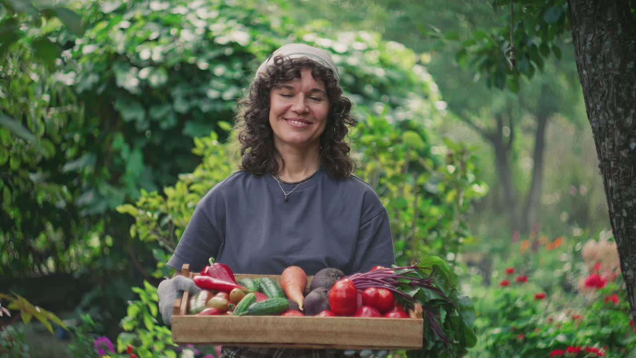 Retrato de una joven sonriente sosteniendo una caja de madera con verduras en un jardín