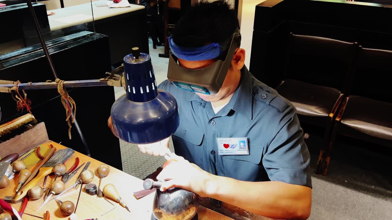 A worker making gold design using tools under the light