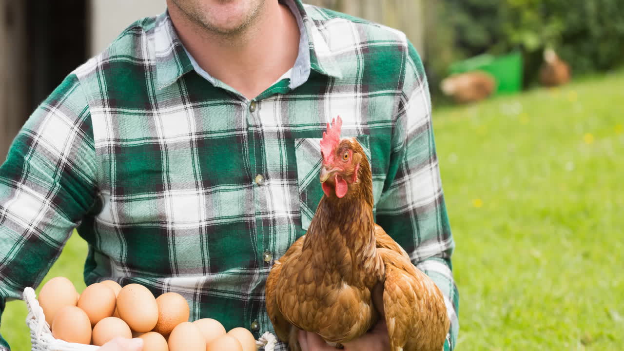 un granjero caucásico sonriente que tiene gallinas y huevos en el patio de la granja