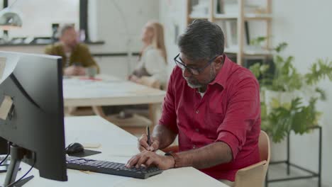 focused indian businessman working on computer and taking notes