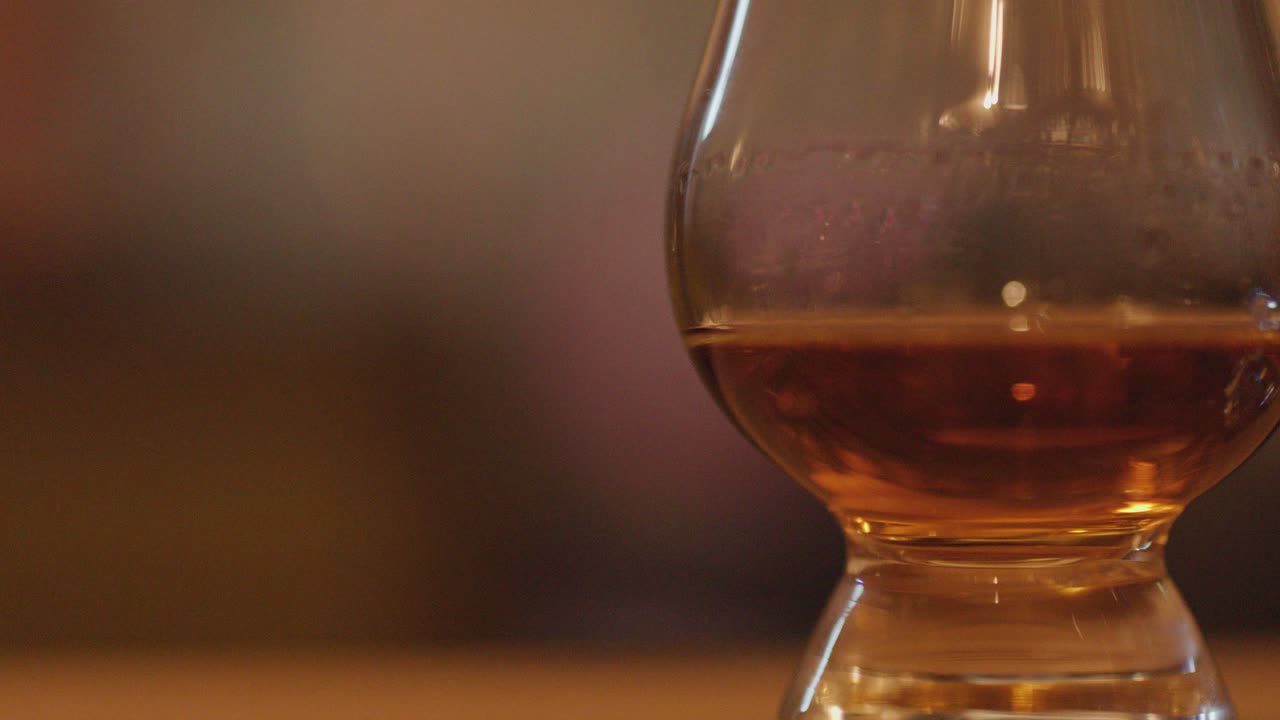 A slow horizontal pan reveals whisky glasses with amber liquid on a wooden table, set against a softly blurred, warmly lit background