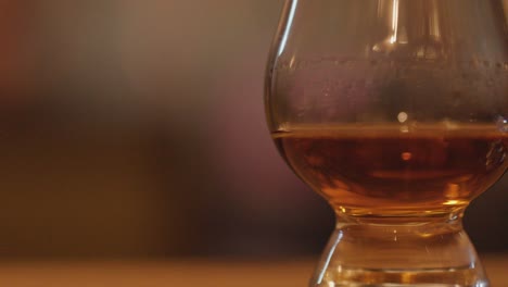 a slow horizontal pan reveals whisky glasses with amber liquid on a wooden table, set against a softly blurred, warmly lit background