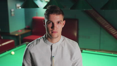 young man in white shirt maintains focused position, holding cue stick in dimly lit pool hall. strategic and intense atmosphere adds depth to moment as player prepares for next move