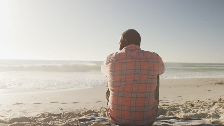 Senior african american man wearing shirt and sitting on sunny beach