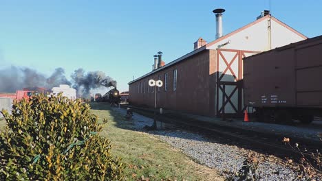 a steam passenger engine arriving into train yard, blowing lots of smoke, puffing along on a sunny winter day