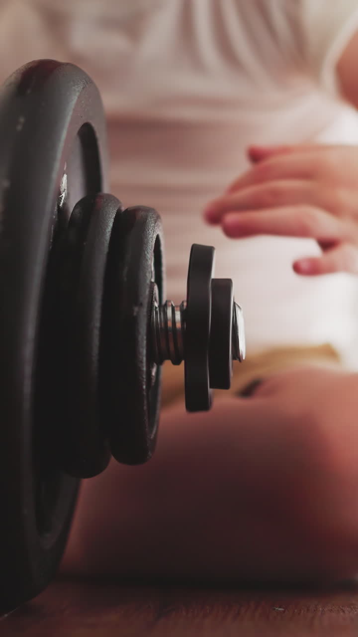 Curious little boy deals with workout barbell sitting on floor in room. Cute child prepares professional equipment for Olympics training closeup slow motion