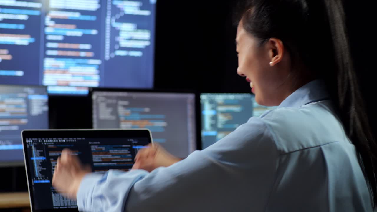 vista de cerca de atrás de una programadora asiática celebrando el éxito de escribir código por una computadora portátil utilizando múltiples monitores que muestran la base de datos en terminales ventanas de escritorio en la oficina
