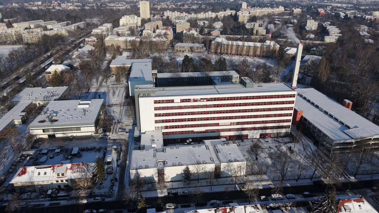 Zimní letecký oblet městského nemocničního komplexu obklopeného zasněženou obytnou čtvrtí a městskými ulicemi v Berlíně, Německo